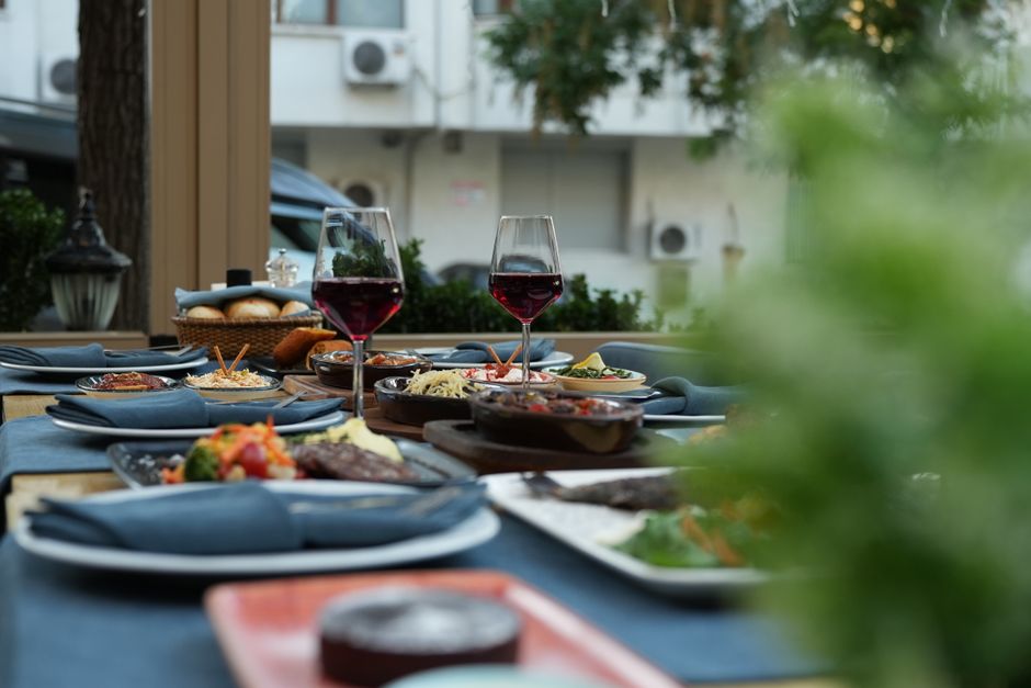 Mesa de jantar ao ar livre com pratos diversos, taças de vinho tinto e ambiente aconchegante, ideal para confraternizações ao ar livre.