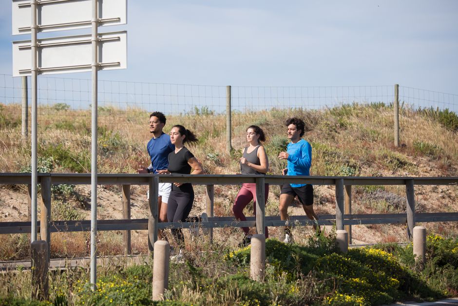 Grupo de pessoas praticando corrida ao ar livre em uma ciclovia com paisagem natural ao fundo.
