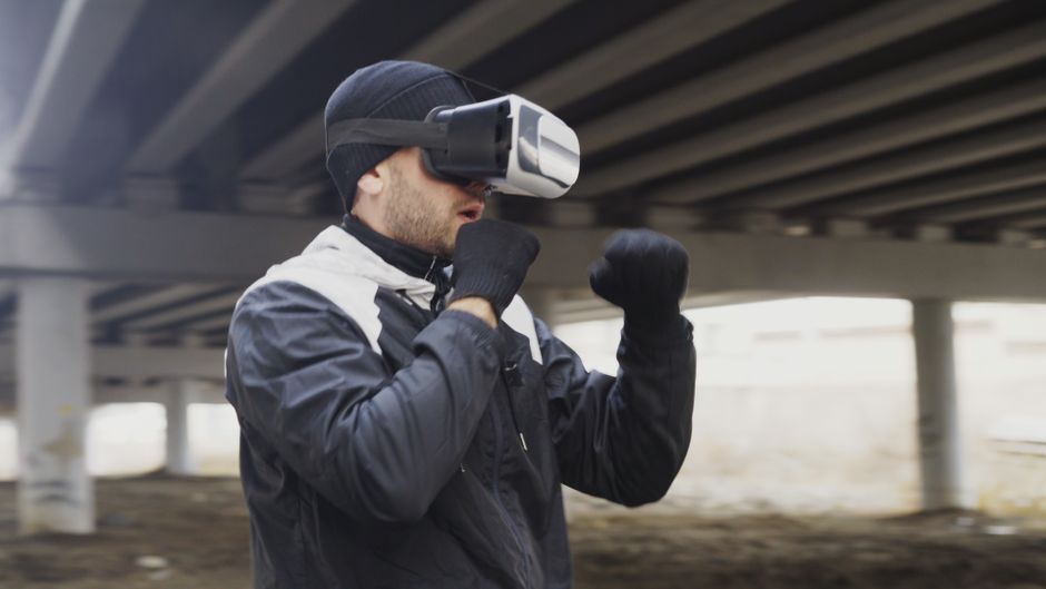 Homem usando óculos de realidade virtual sob uma ponte, explorando tecnologias imersivas ao ar livre.