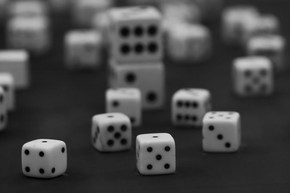 Imagem de dados de jogos de azar com dados de diferentes tamanhos espalhados em uma superfície escura, destacando o tema de jogos e apostas.