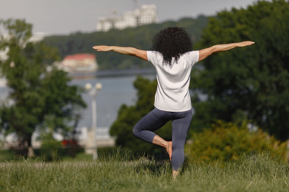 Mulher praticando yoga ao ar livre, representando bem-estar e equilíbrio.