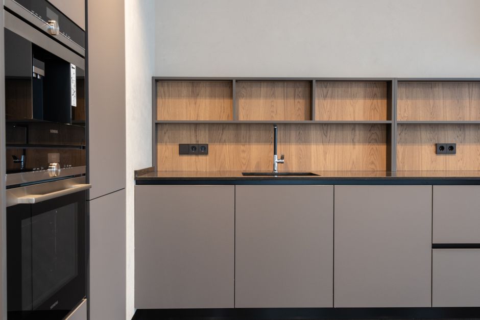 Imagem de uma área de cozinha moderna, com armários cinza e detalhes em madeira, ideal para ilustrar ambientes de coworking ou espaços de convivência em escritórios.