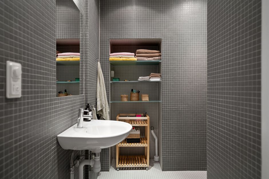 Imagem de um banheiro organizado com parede de azulejos pequenos, espelho, pia, prateleiras com toalhas, cestas e itens de higiene, ideal para ilustrar organização doméstica ou design de interiores.