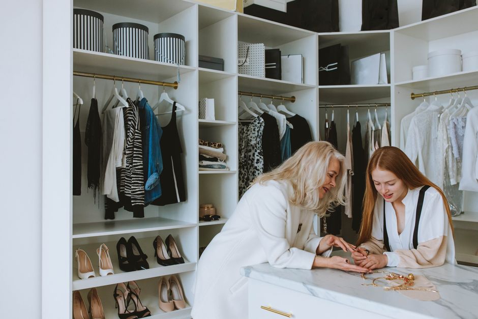 Duas mulheres discutindo escolhas de roupas e acessórios em um closet organizado, com foco na moda e estilo pessoal.