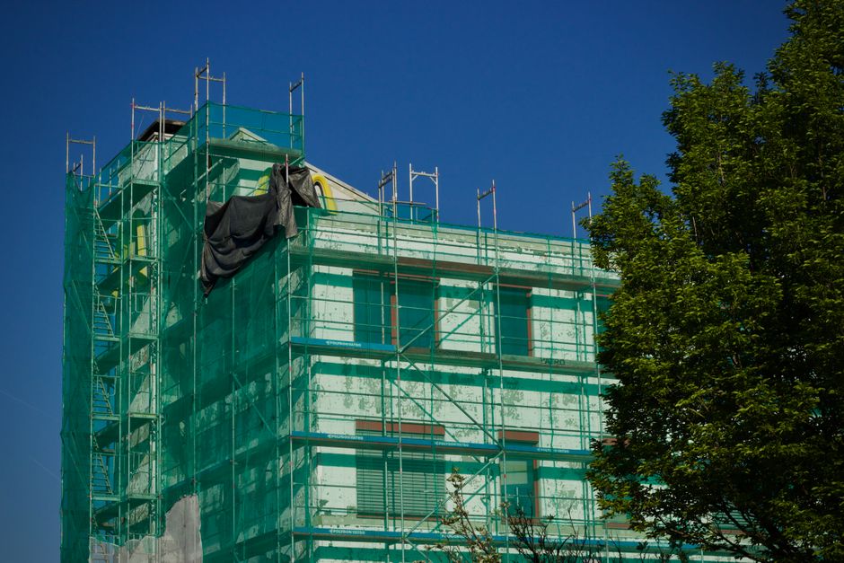 Imagem de um edifício em construção com escada de andaimes e tela de proteção sob um céu azul claro.