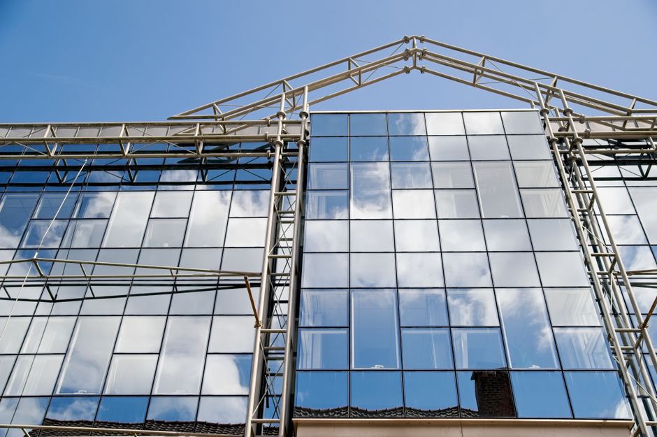 Fachada de um edifício moderno com estrutura de aço e espelhos de vidro refletindo o céu e as nuvens, simbolizando inovação e design arquitetônico.