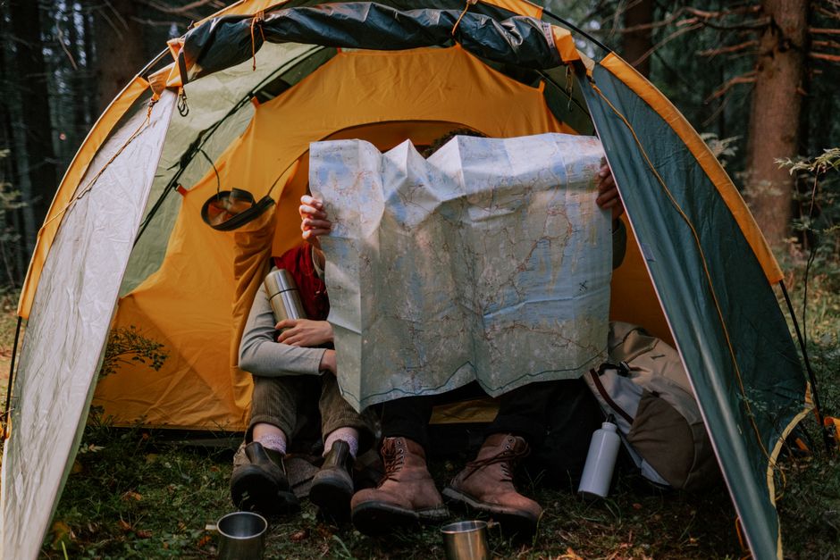 Pessoa com mochila e mapa dentro de uma barraca de camping em uma floresta, explorando a natureza e planejando uma aventura ao ar livre.