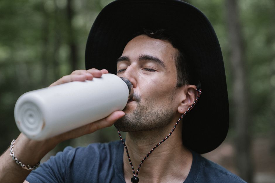 Homem desfrutando de uma bebida enquanto está ao ar livre em um ambiente natural, transmitindo uma sensação de relaxamento e conexão com a natureza.