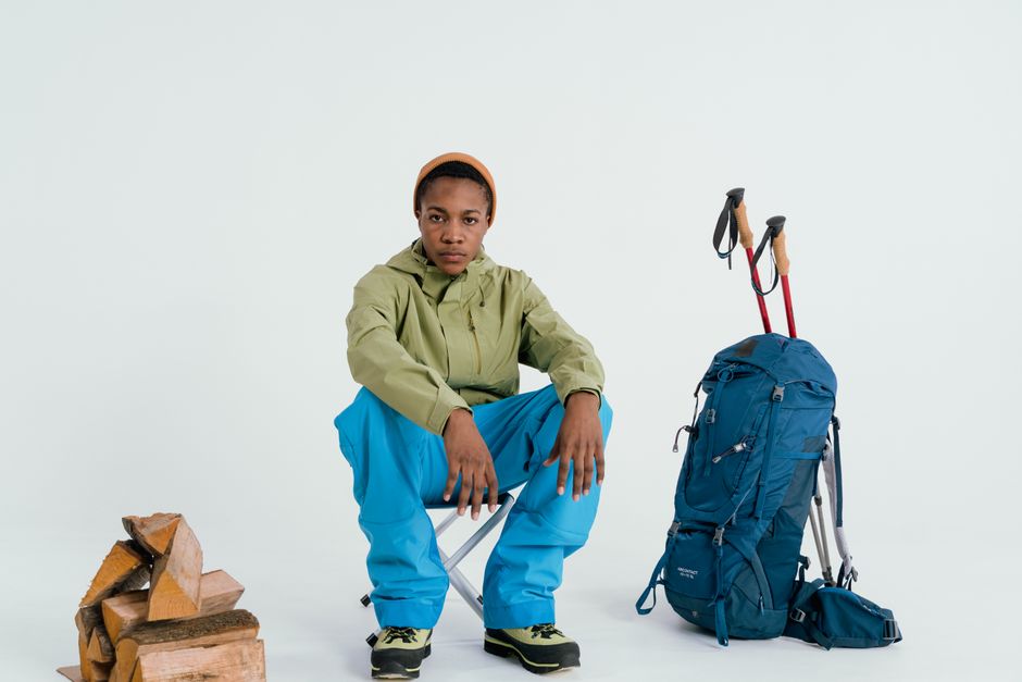 Jovem aventureira em roupas de trilha, com mochila e bastões de caminhada ao lado, pronta para uma viagem ou expedição ao ar livre.