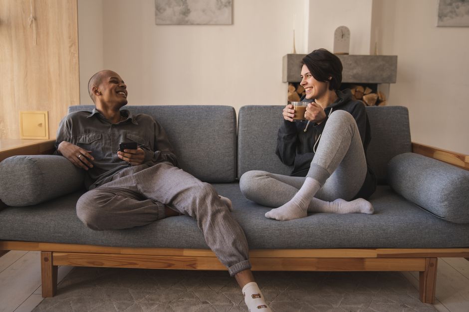 Duas pessoas conversando e sorrindo confortavelmente em um sofá, transmitindo uma atmosfera de convivência e bem-estar em ambiente doméstico.