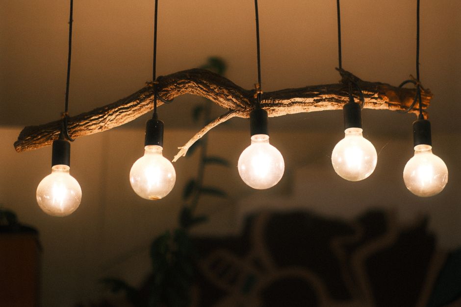 Lustre decorativo feito com galho de árvore e lâmpadas de vidro, criando uma iluminação ambiente aconchegante e rústica.