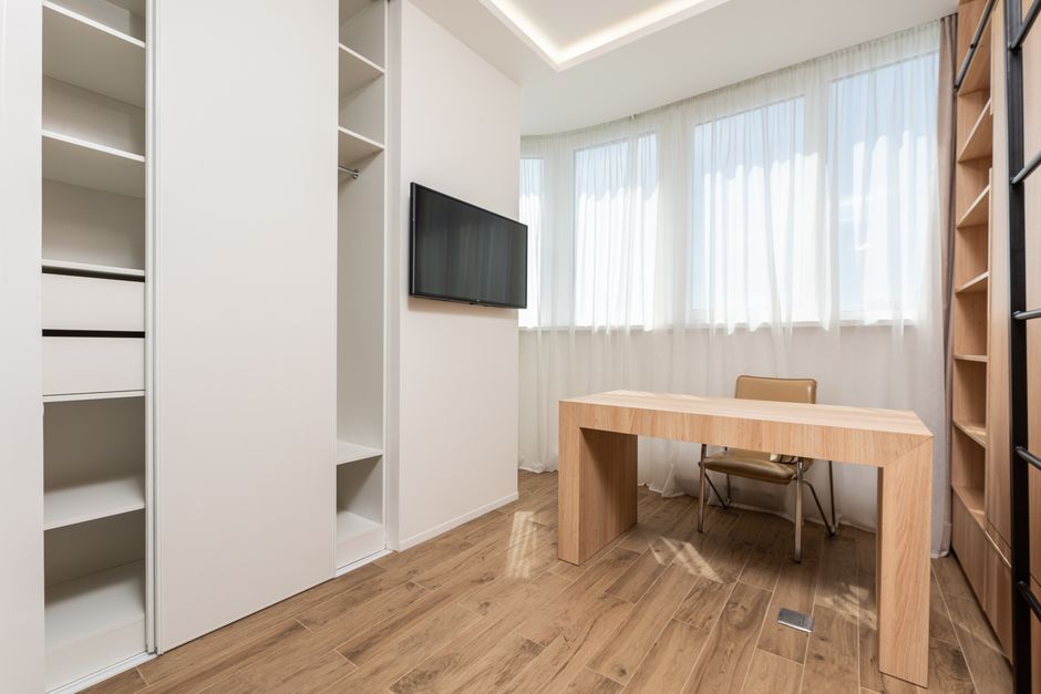 Sala de escritório minimalista com iluminação natural, mesa de madeira e televisão, ideal para ambientes de trabalho e estudos.
