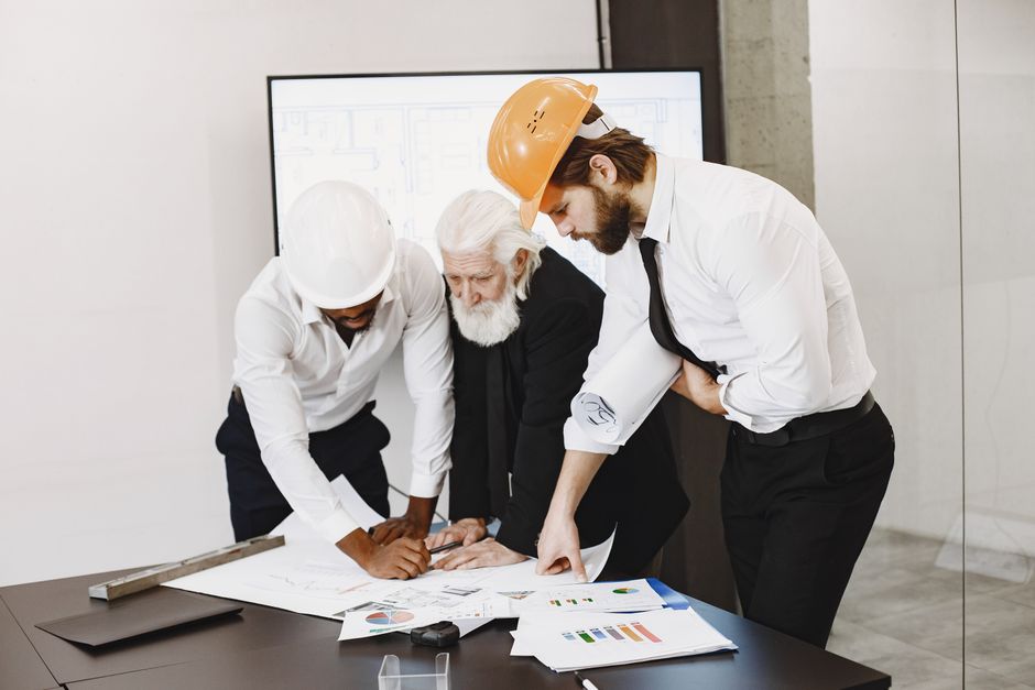 Equipe de engenheiros e um consultor analisando projetos em uma reunião de planejamento de construção civil.