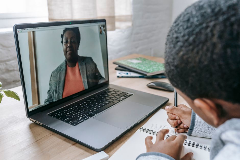 Pessoa participando de uma reunião virtual ou entrevista online, com uma tela de computador exibindo outra pessoa ao centro da imagem.