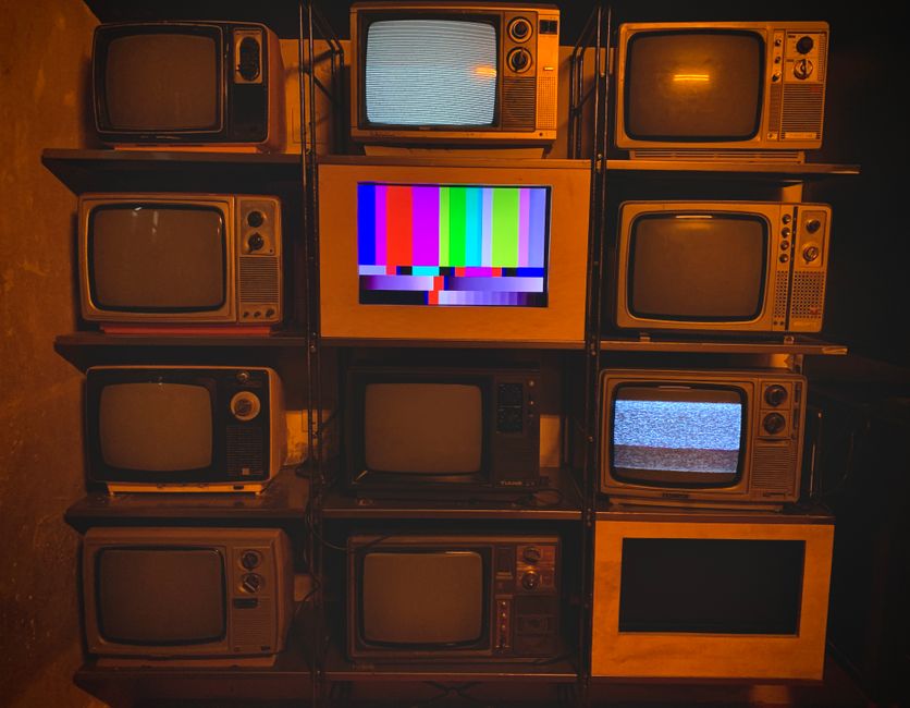 Coleção de televisores antigos ligados a uma estrutura em um ambiente de estética vintage ou retrô.
