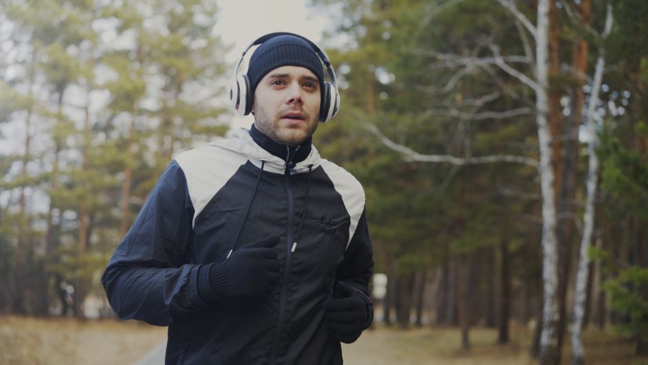 Homem praticando corrida ao ar livre em meio à natureza, vestindo roupas de esporte e fones de ouvido.
