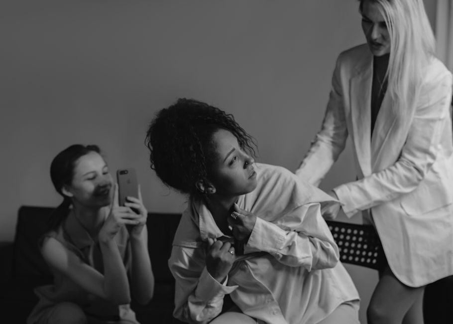 Imagem de uma consulta médica com uma profissional examinando uma paciente, enquanto outra mulher na sessão tira fotos.