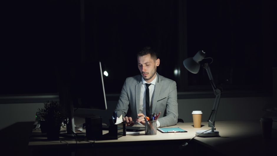 Homem de terno trabalhando à noite em ambiente de escritório, focado em suas tarefas com iluminação suave, transmitindo produtividade após o expediente.