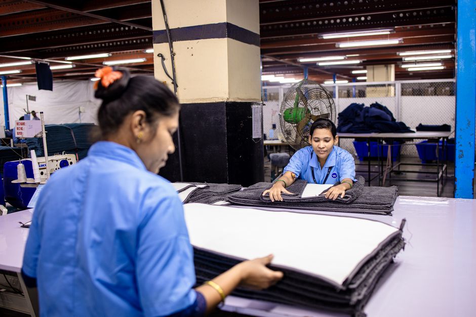 Duas funcionárias trabalhando na confecção de uniformes ou roupas em uma fábrica, focando na produção e coordenação do trabalho.