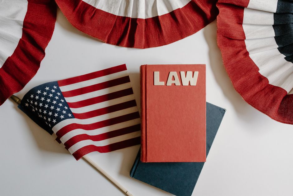 Imagem com tema de direito e celebração patriótica, destacando uma bandeira dos Estados Unidos, uma agitação de papel colorido e livros sobre legislação.