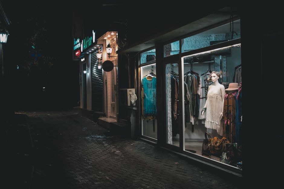 Vitrine de loja de roupas feminina iluminada à noite, exibindo peças e acessórios em destaque.