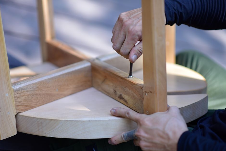 Pessoa montando uma cadeira de madeira, focada no processo de fabricação artesanal de móveis.