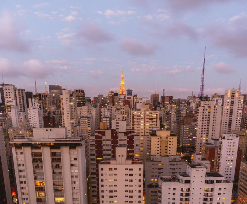 Vista panorâmica de uma cidade vibrante ao entardecer, evidenciando o skyline urbano e o céu com nuvens coloridas