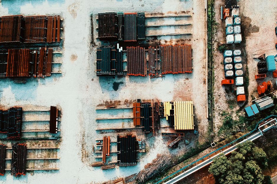 Imagem aérea de um depósito de materiais de construção, destacando a organização de tubulações e equipamentos industriais.