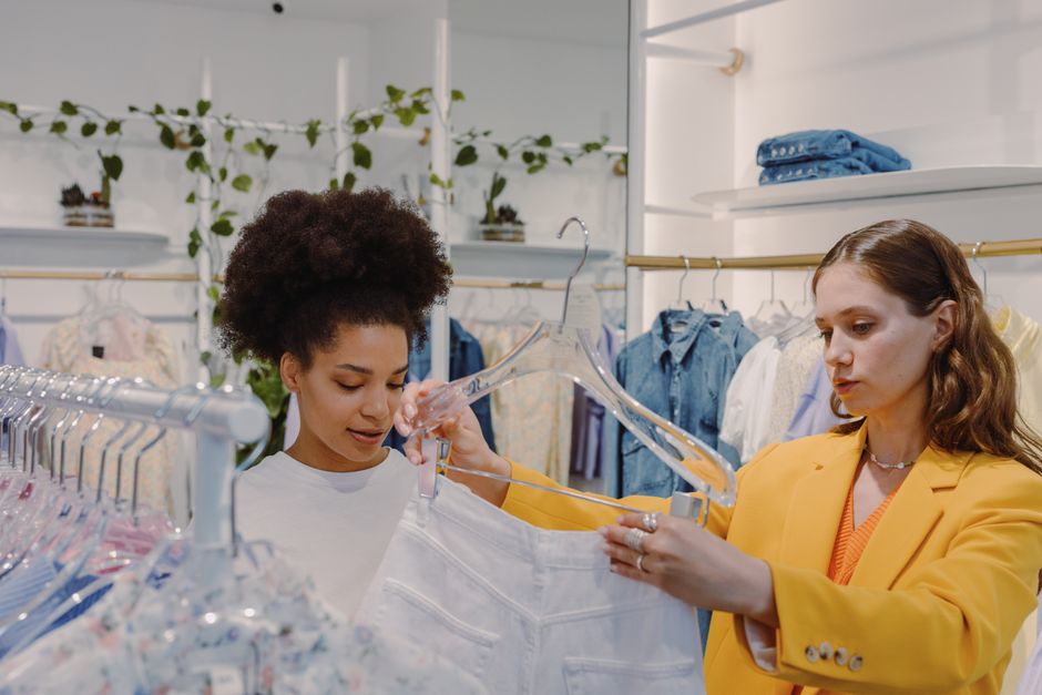 Duas mulheres explorando roupas em uma loja, destacando o tema de moda e consumo feminino.
