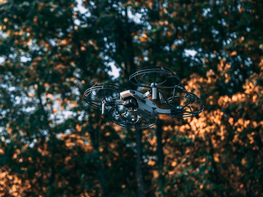 Imagem de um drone em voo ao entardecer com o céu e árvores ao fundo, simbolizando inovação e tecnologia ao ar livre.