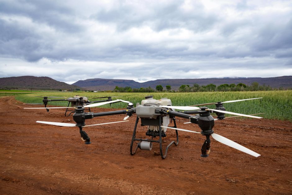 Drone agrícola realizando monitoramento de lavoura em campo aberto sob céu nublado.
