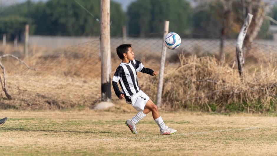 Menino jogando futebol em um campo ao ar livre, focado na prática esportiva infantil.