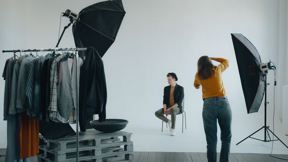 Sessão de fotos em um estúdio com modelo sentado, preparação de look e iluminação profissional, ideal para conteúdo de moda ou produção de fotos.