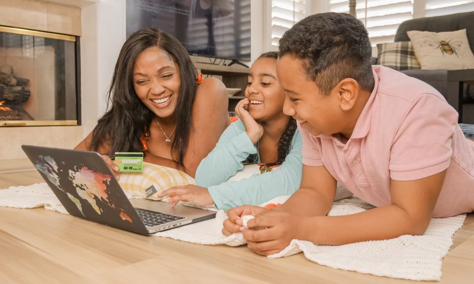 Família assistindo a vídeo chamada ou programa de vídeo no laptop, simbolizando conexão e momentos de lazer em casa.
