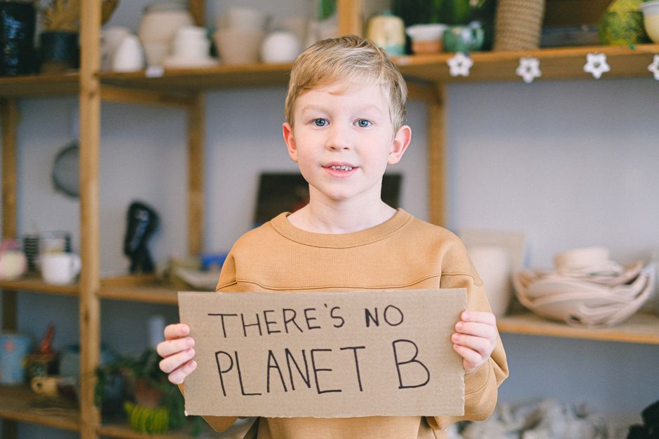 Criança em ato de conscientização ambiental segurando cartaz com mensagem sobre mudanças climáticas.