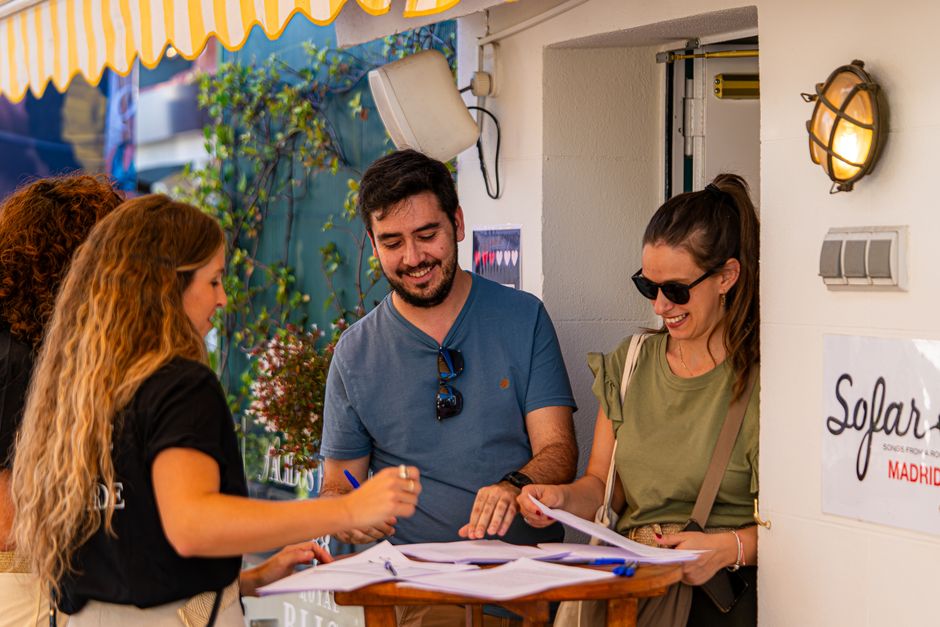 Grupo de pessoas conversando e sorrindo ao redor de uma mesa ao ar livre, em ambiente de lazer ou evento social, com decoração e iluminação acolhedora.