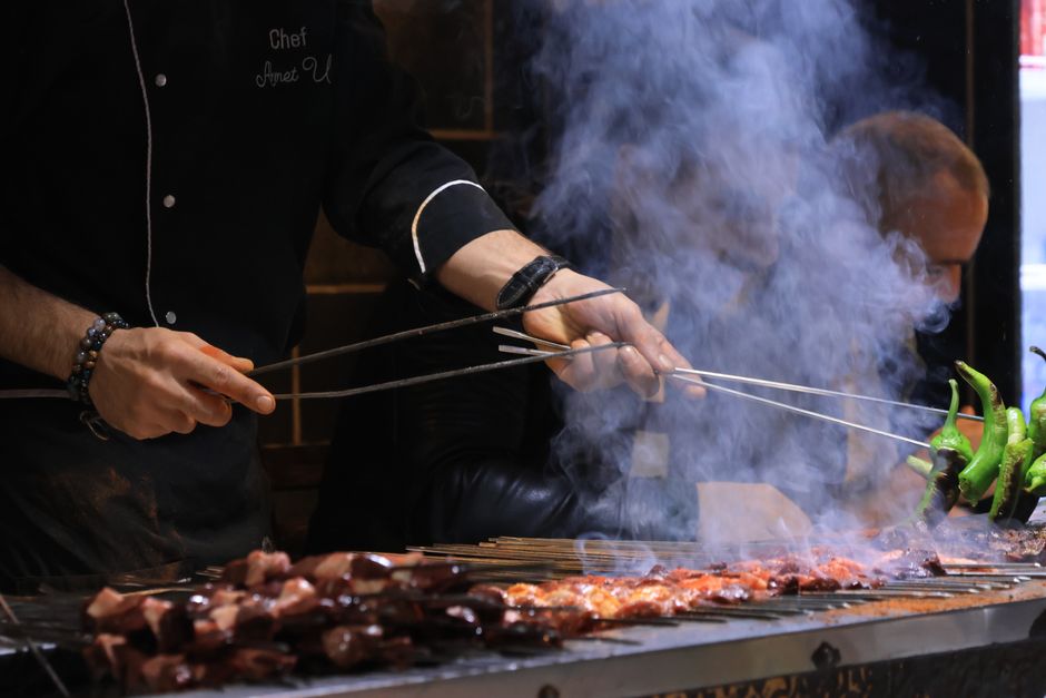 Chef preparando churrasco na grelha com fumaça, destacando o uso de técnicas de churrasco em ambiente gastronômico.