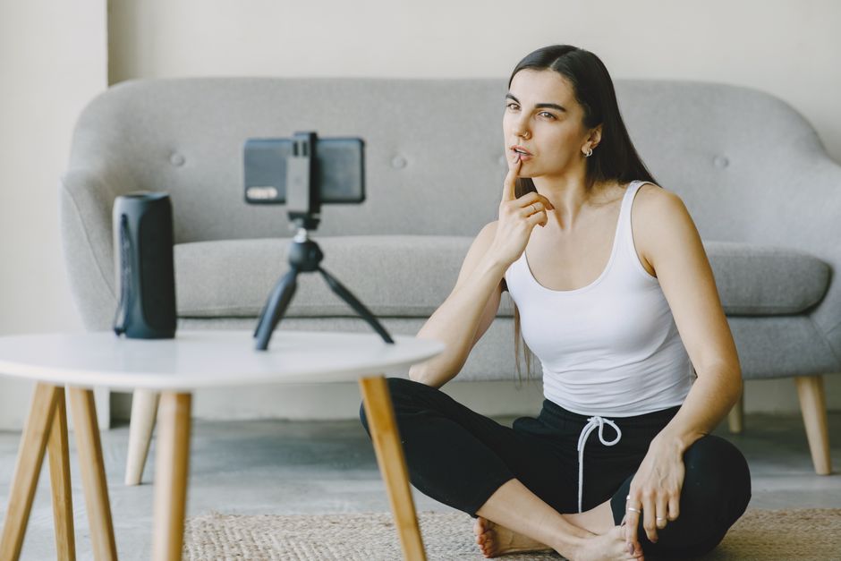 Mulher fazendo um vídeo para o blog, em um ambiente confortável e caseiro, usando um celular conectado a um tripé para gravação.