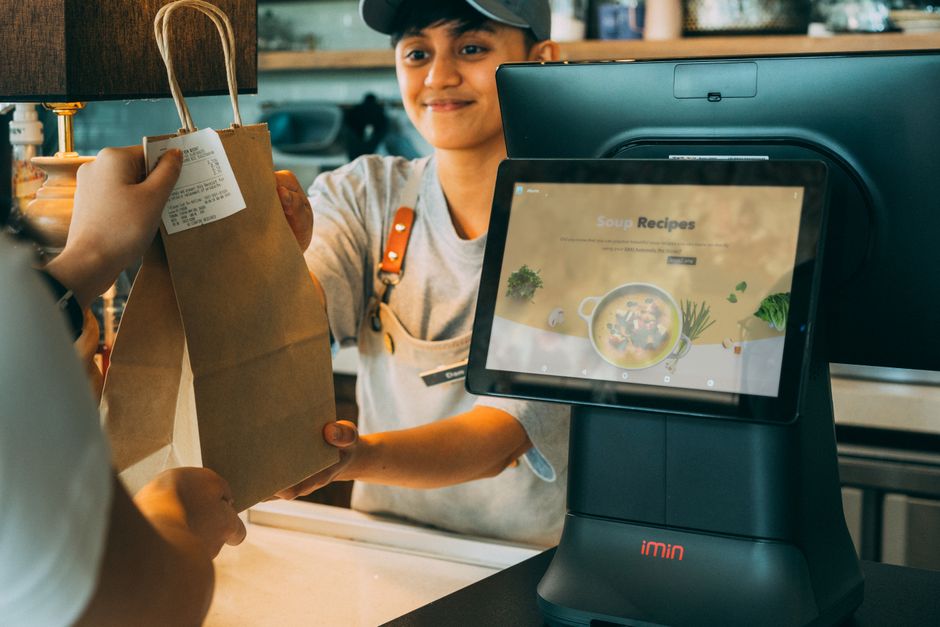 Pessoa fazendo um pedido em um café usando um sistema de autoatendimento digital, destacando inovação no atendimento ao cliente.