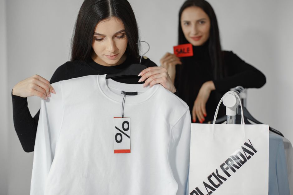 Duas mulheres aproveitando uma liquidação de roupas e promoções de Black Friday em uma loja de moda.