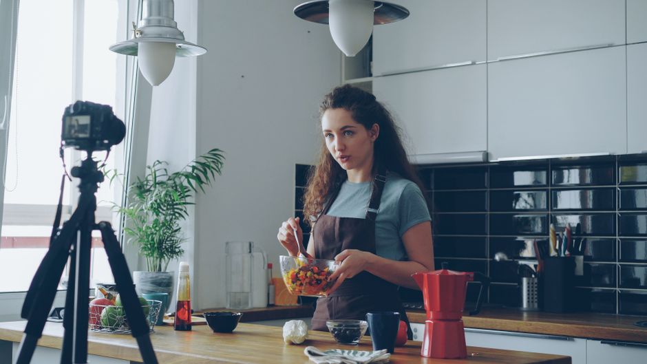 Mulher preparando uma receita de comida em uma cozinha moderna enquanto grava um vídeo para o blog.
