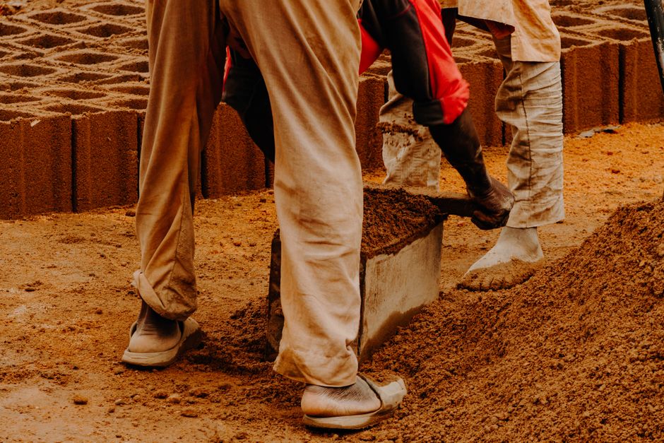 Homens trabalhando na construção de um muro de tijolos na obra civil ao pôr do sol.