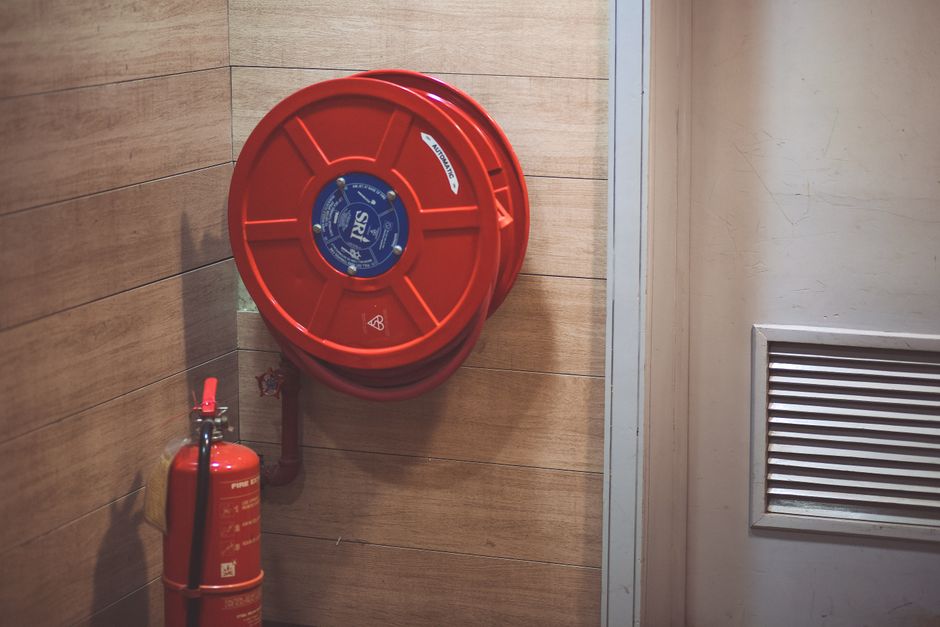 Imagem de um extintor e mangueira de incêndio instalados em uma parede de ambiente corporativo, simbolizando segurança contra incêndios.