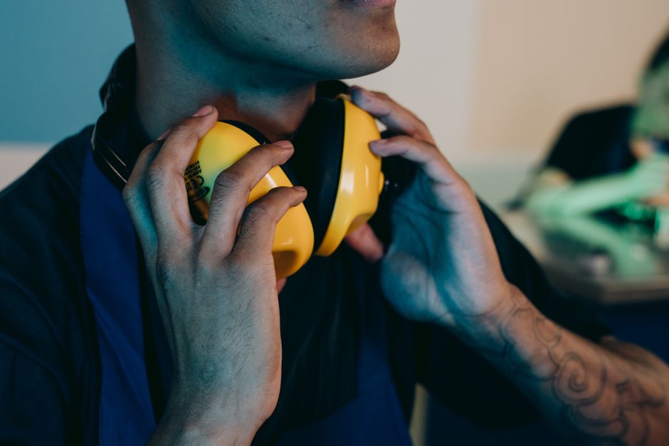 Homem ajustando fones de ouvido com fone de segurança amarelo em um ambiente de trabalho, sugerindo foco, concentração ou preparação para uma tarefa.