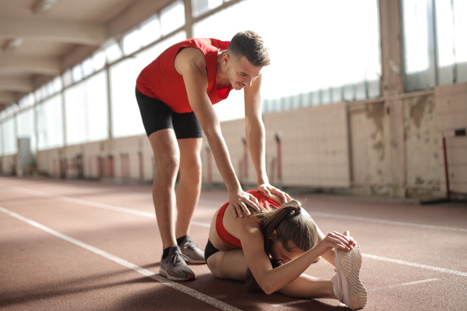 Atleta ajudando uma colega a se recuperar após uma corrida de pista indoor, demonstrando cuidado e apoio esportivo.
