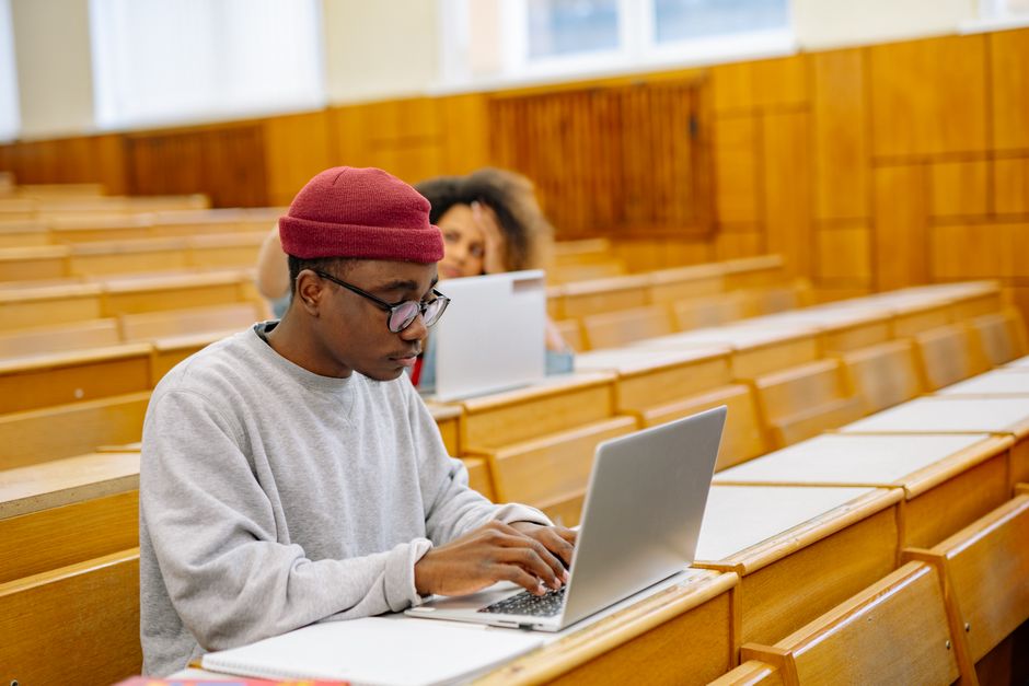 Estudante usando laptop em sala de aula acadêmica, em um ambiente de estudos e aprendizado.