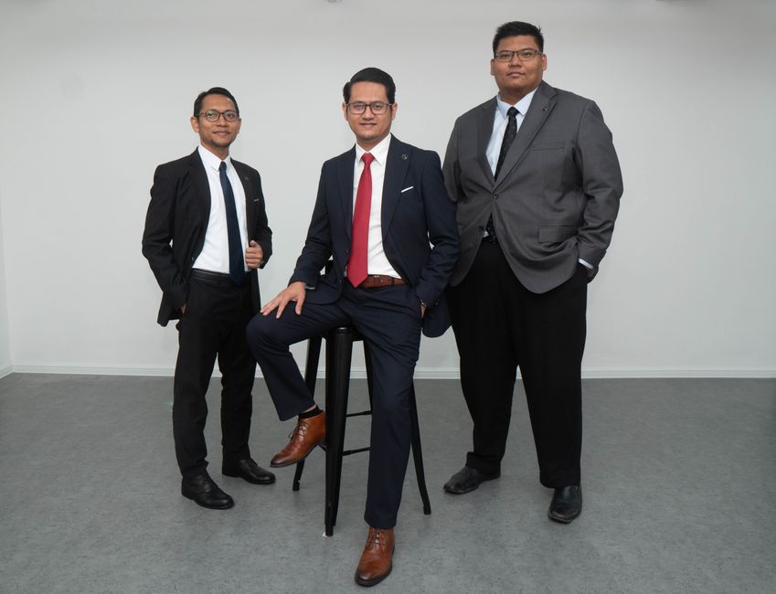 Três profissionais de terno posando em um ambiente formal, simbolizando liderança e confiança nos negócios.