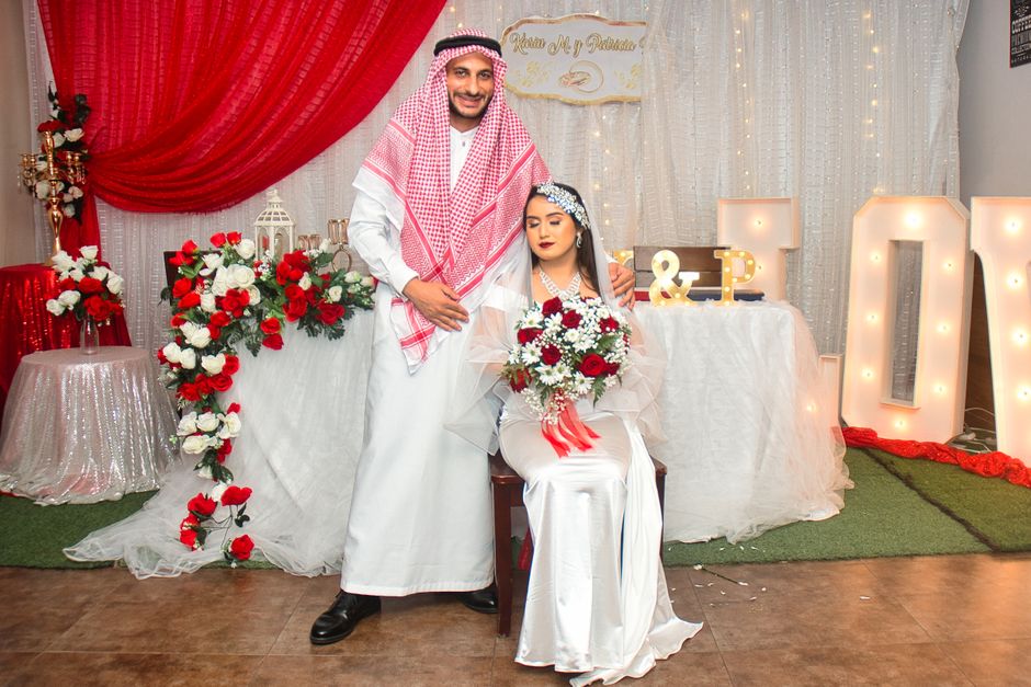 Casal em cerimônia de casamento tradicional, com decoração elegante em tons de vermelho e branco, destacando a celebração do matrimônio.