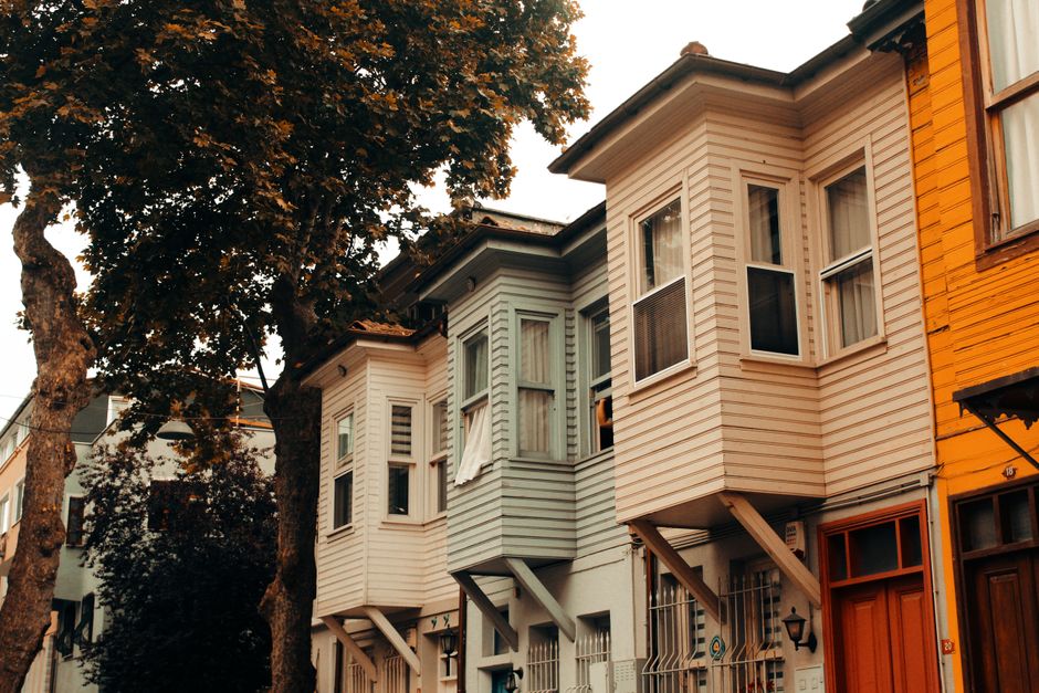 Casas tradicionais de estilo vitoriano em uma rua urbana, com árvores ao fundo, retratando a arquitetura residencial clássica.