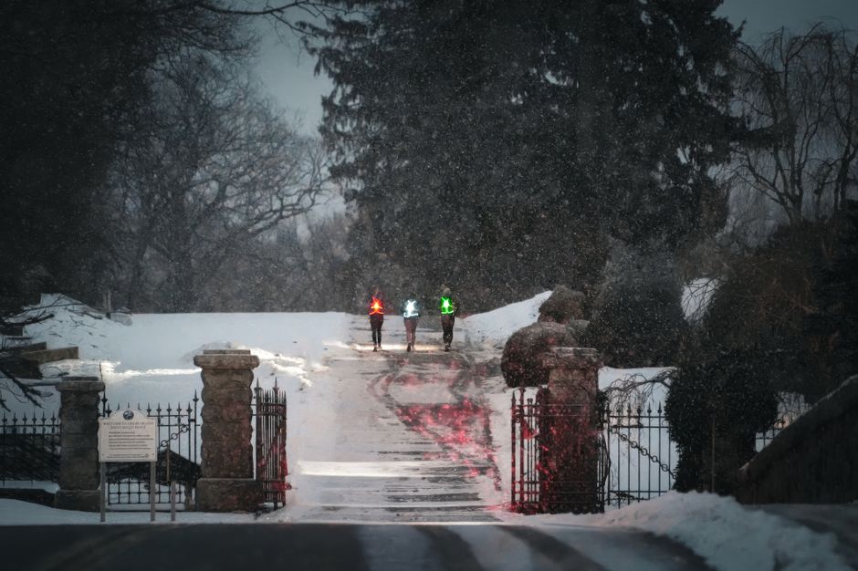 Caminho com três pessoas usando faróis de sinalização coloridos em uma noite de inverno com neve, destacando a segurança e a orientação em condições adversas.